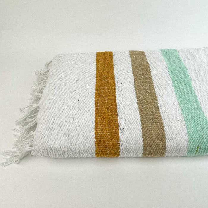 The Sol Throw is woven from 100% post consumer fibers. Bold seafoam green, tan and rust stripes frame each end, finished with hand twisted fringe. Sustainability meets modern California style. Measures 74" x  51"