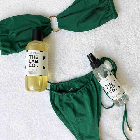 GREEN BIKINI LAID ON A TOWEL WITH TLC SPORTS DETERGENT AND FABRIC MIST NEXT TO IT