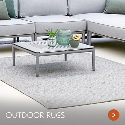 A wooden bench rests on a cream outdoor rug