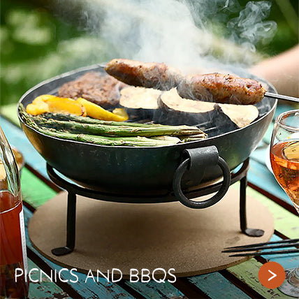 A sturdy metal bowl with sizzling food on a picnic table