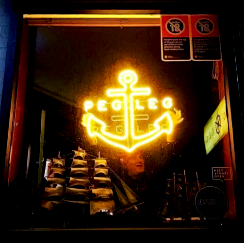 Tyrone M's testimonial image showing a custom gold LED neon sign with an anchor design in a business window display. The bright lighted LED sign grabs customers' attention and helps improve foot traffic to the store.