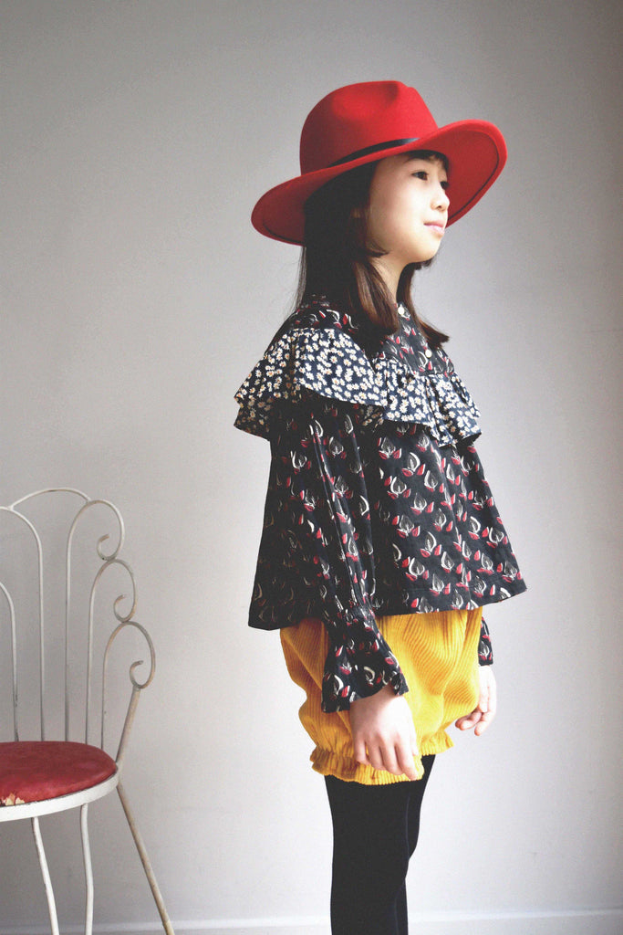 lulaland Fall No.15 Mirage collection. Girl wearing a black ruffled blouse with leafy print and yellow corduroy bloomers. Organic girl's clothes