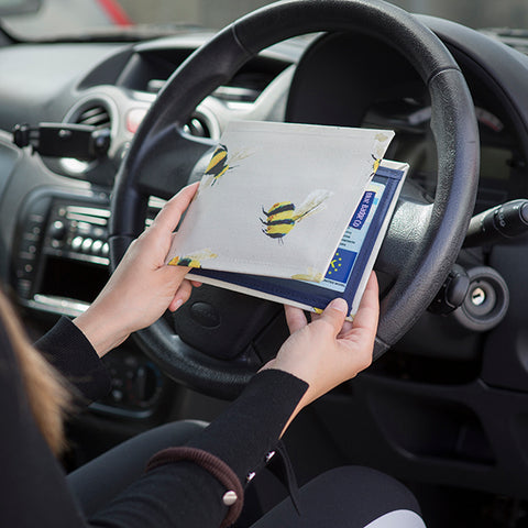 Woman holding a Blue Badge Wallet with bees design in front of the steering wheel inside a car