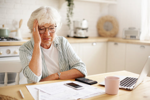 Distressed older woman with calculator and laptop trying to organise budget