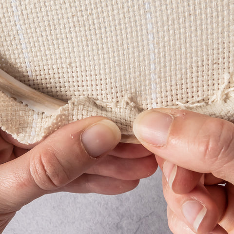 Hands securing fabric onto glued hoop edge