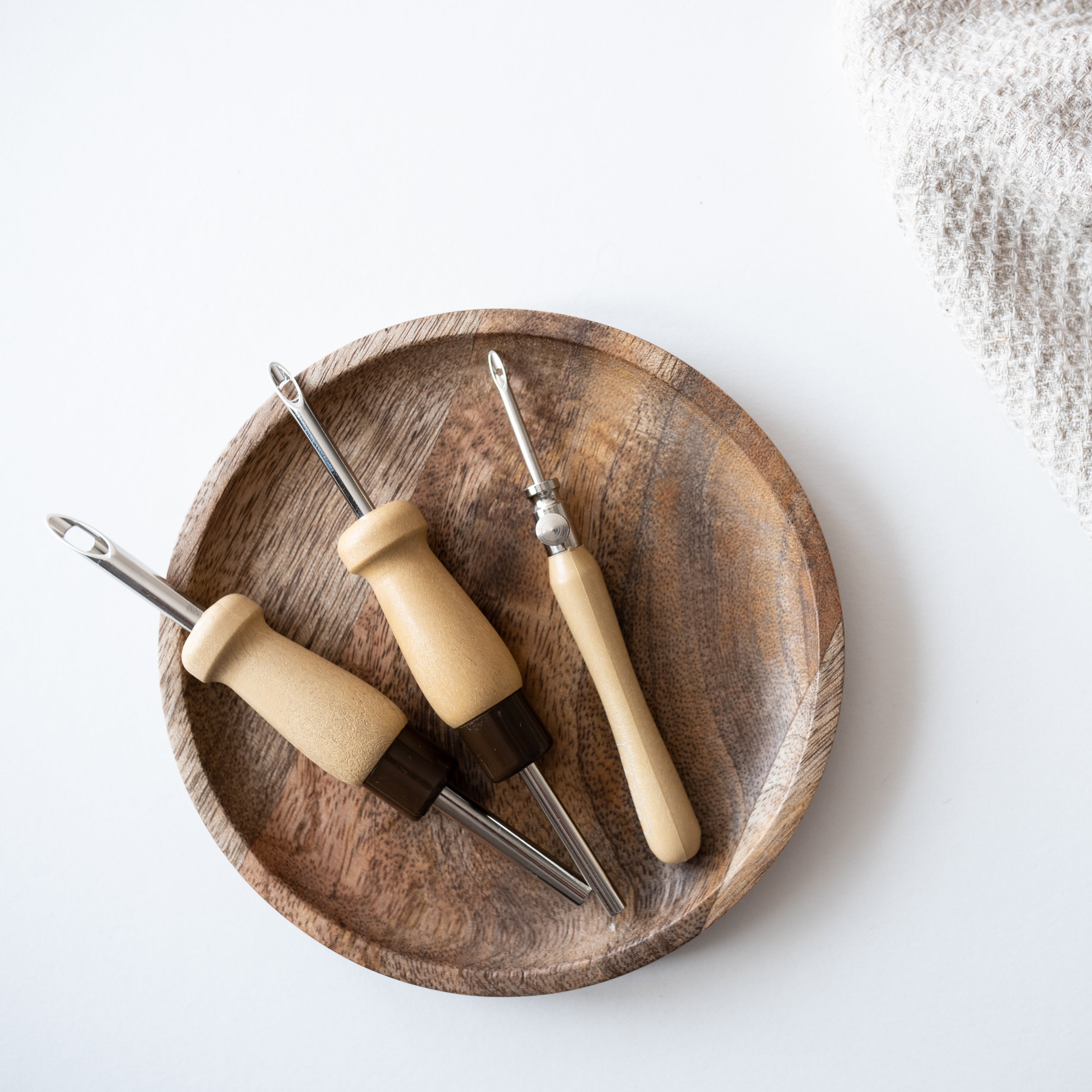 Three Lavor punch needle tools on a small wooden dish, fabric just coming into shot in the corner