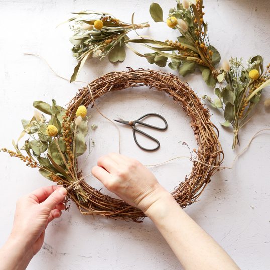 Hands tying string around flowers on a handmade wreath