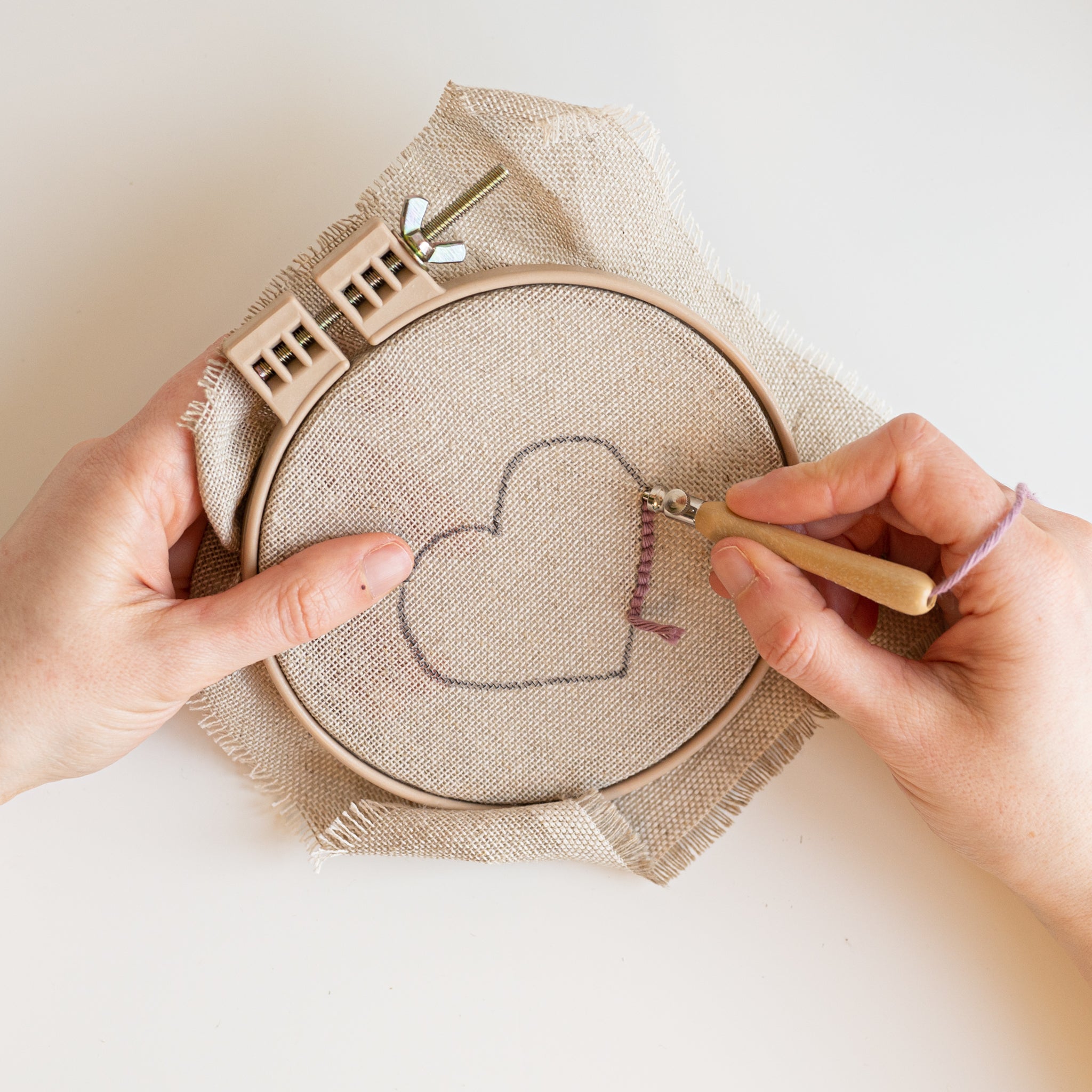 Hands holding a hoop stretched with linen making a punch needle heart using a Lavor punch needle