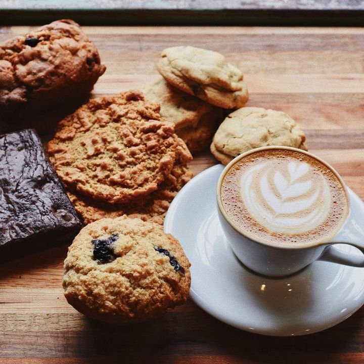Photo of a cappuccino on a saucer next to an assortment of baked goods.