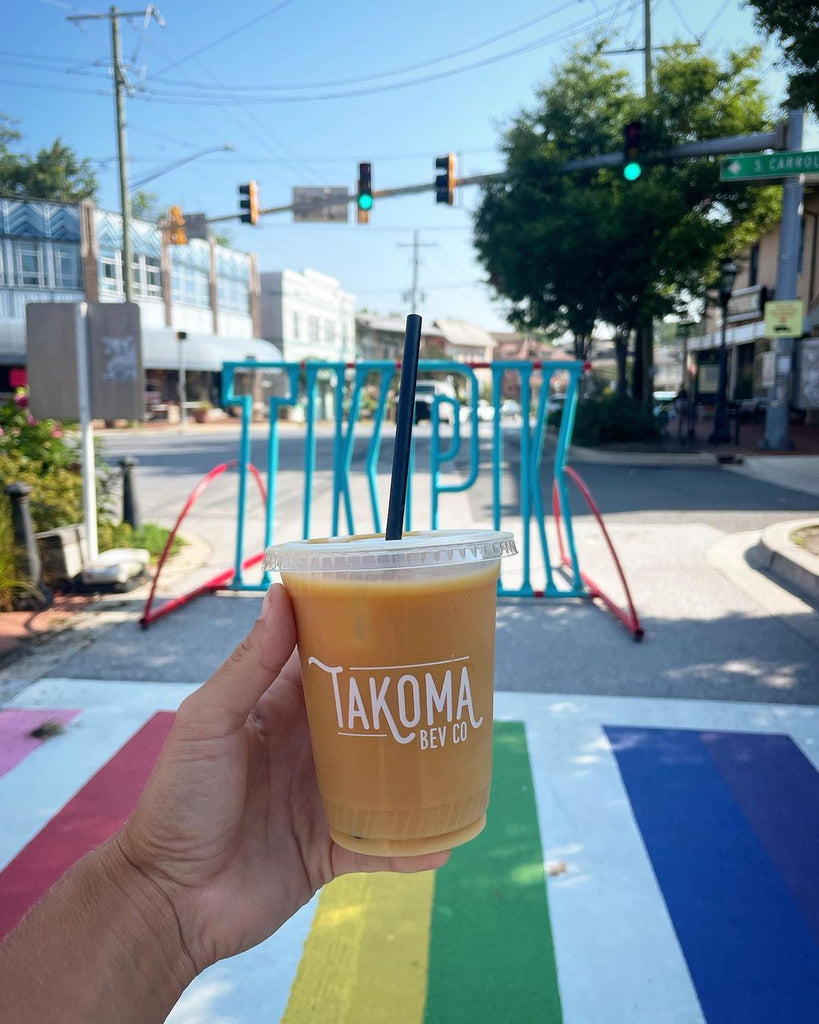 Photo of a hand holding out a to-go cup that says, "Takoma" outside.
