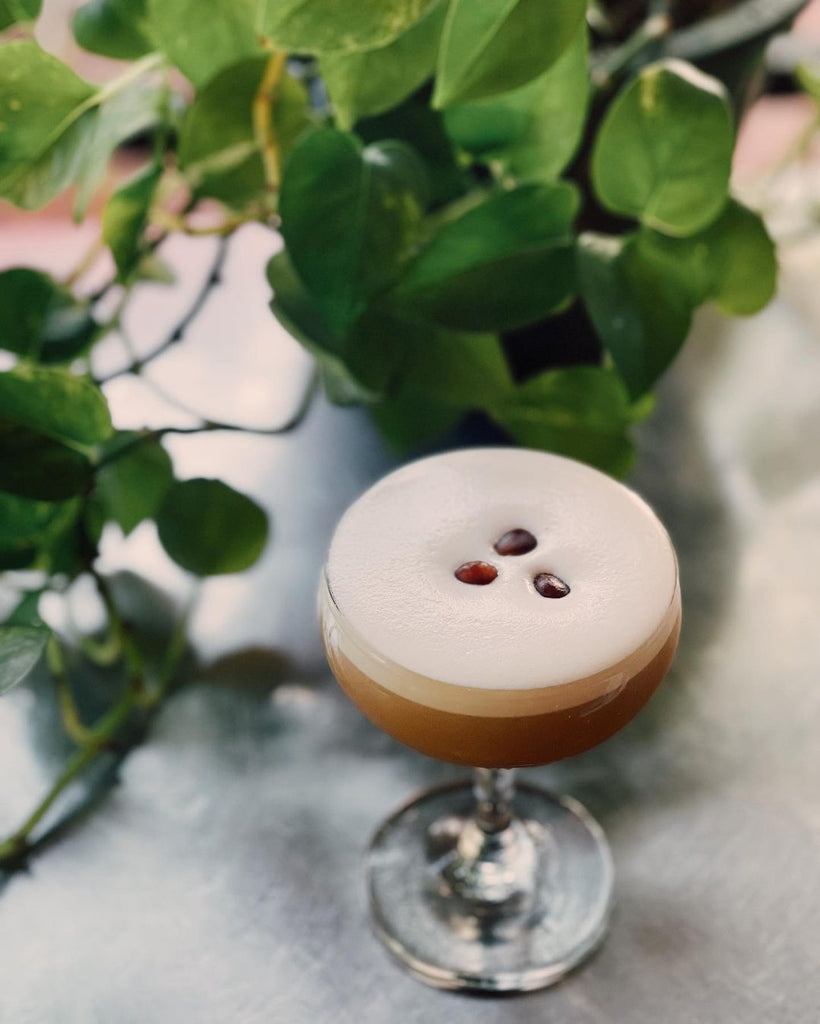 Photo of an espresso martini sitting on a ledge. There are three coffee beans resting on the foam.