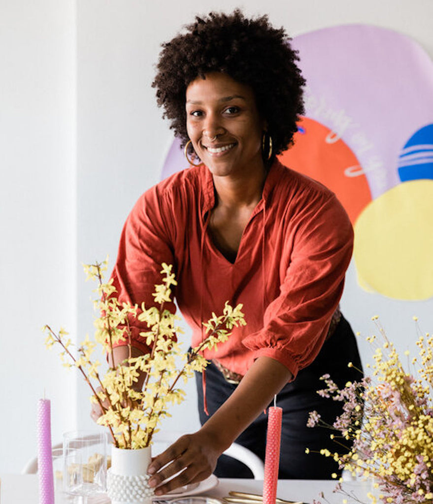 Photo of Whit smiling at the camera while arranging flowers in a vase.