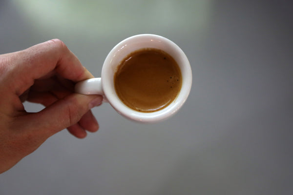 Photo of a hand holding a demitasse cup of espresso.