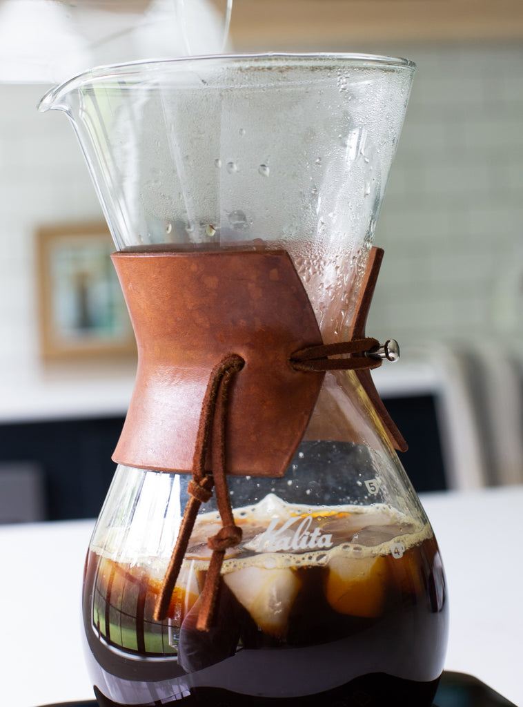 Photo of a chemex with a leather wrap sitting on a scale in a kitchen.
