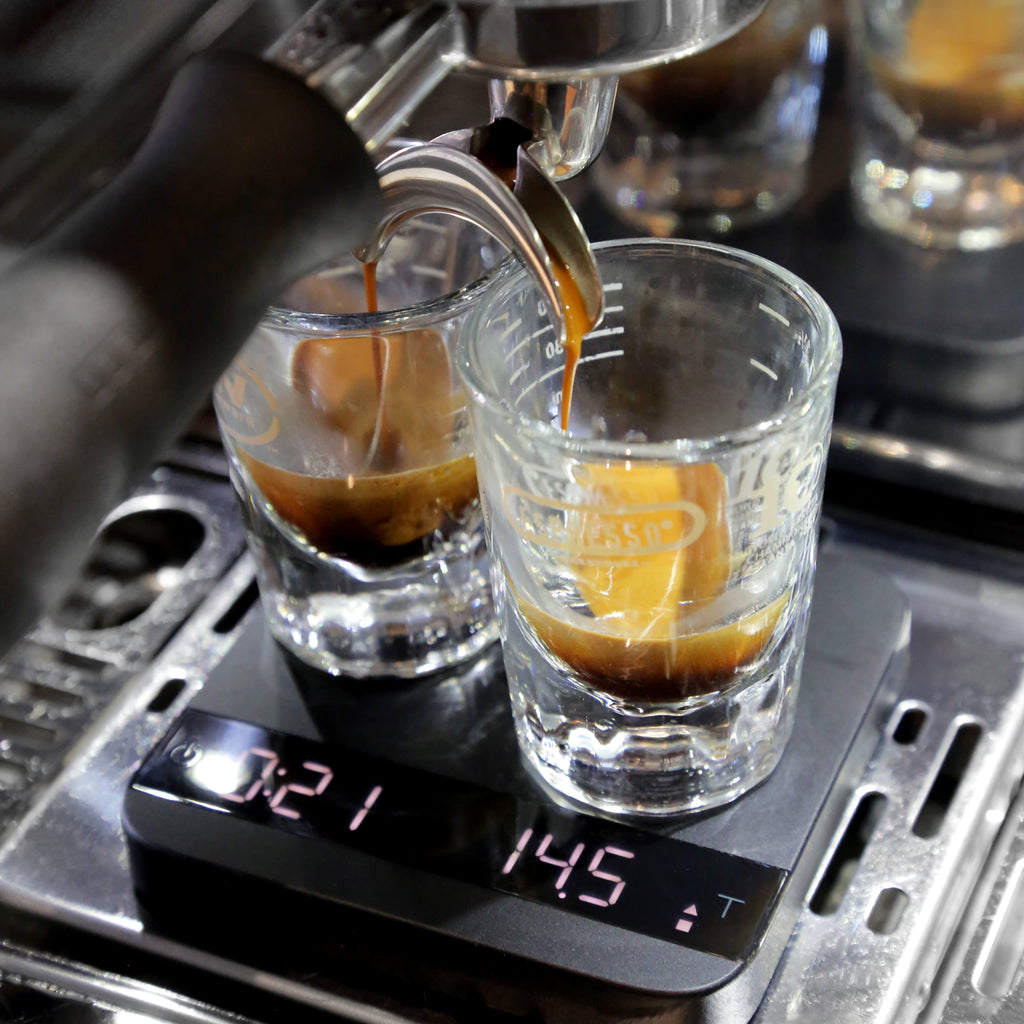 Photo of espresso pouring into two small glasses on a scale.