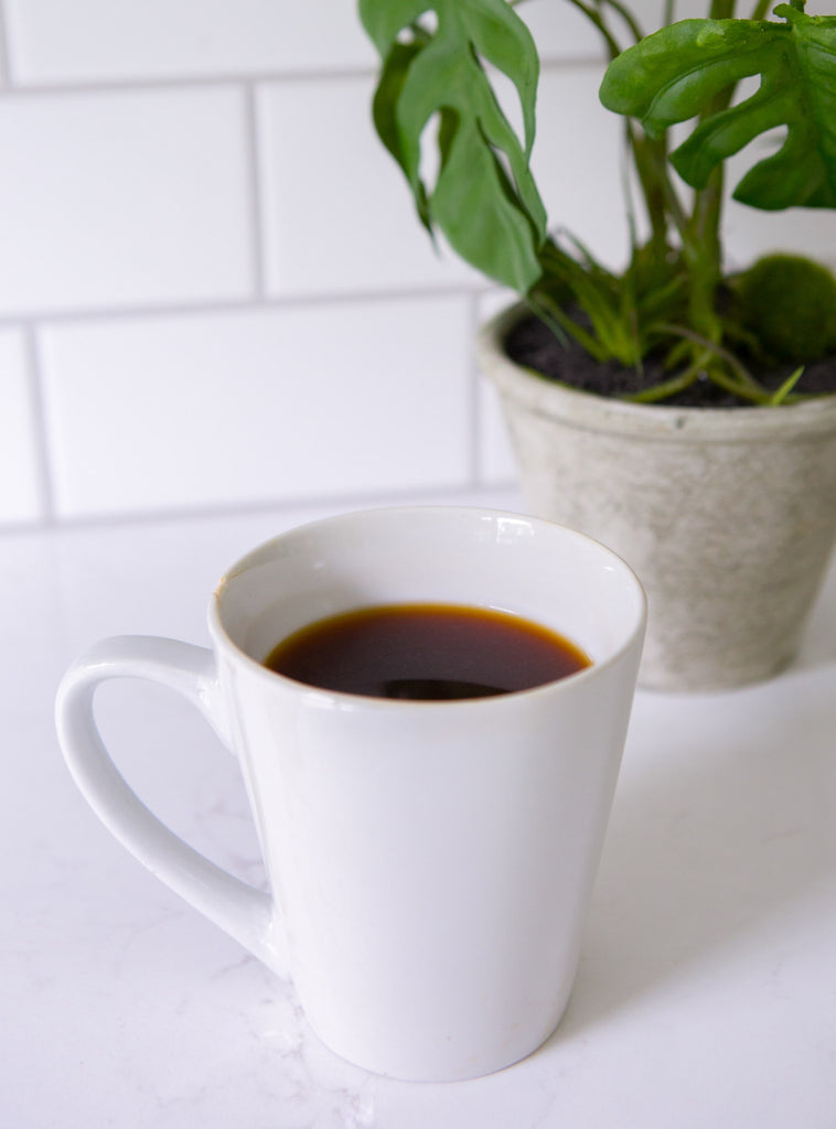Photo of a mug of coffee in front of a plant on a kitchen counter.