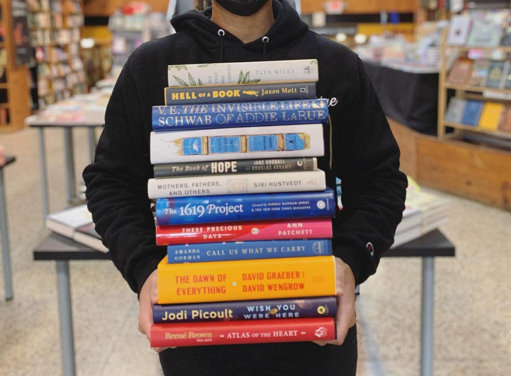 Photo of a person holding a stack of 12 books in front of them.