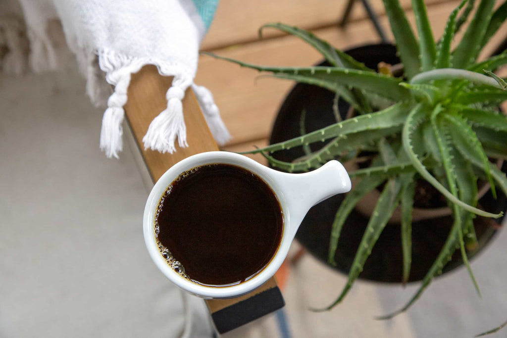 Photo of a mug of coffee on a wooden surface next to an aloe vera plant.