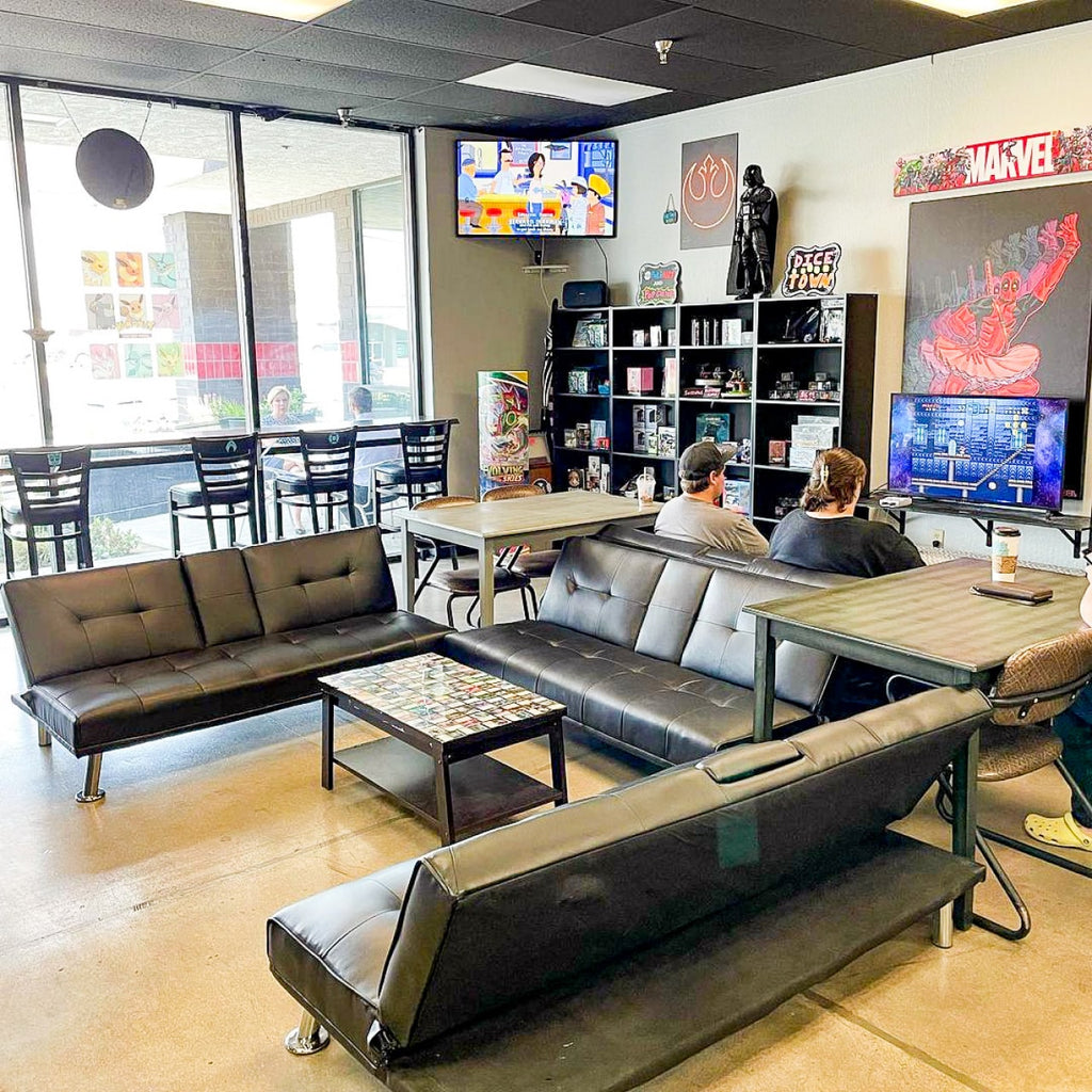 Photo of the inside of Coffee N' Comics. There is a horseshoe shaped arrangement of couches, a TV in the corner, and shelves with items from movies and comic books.