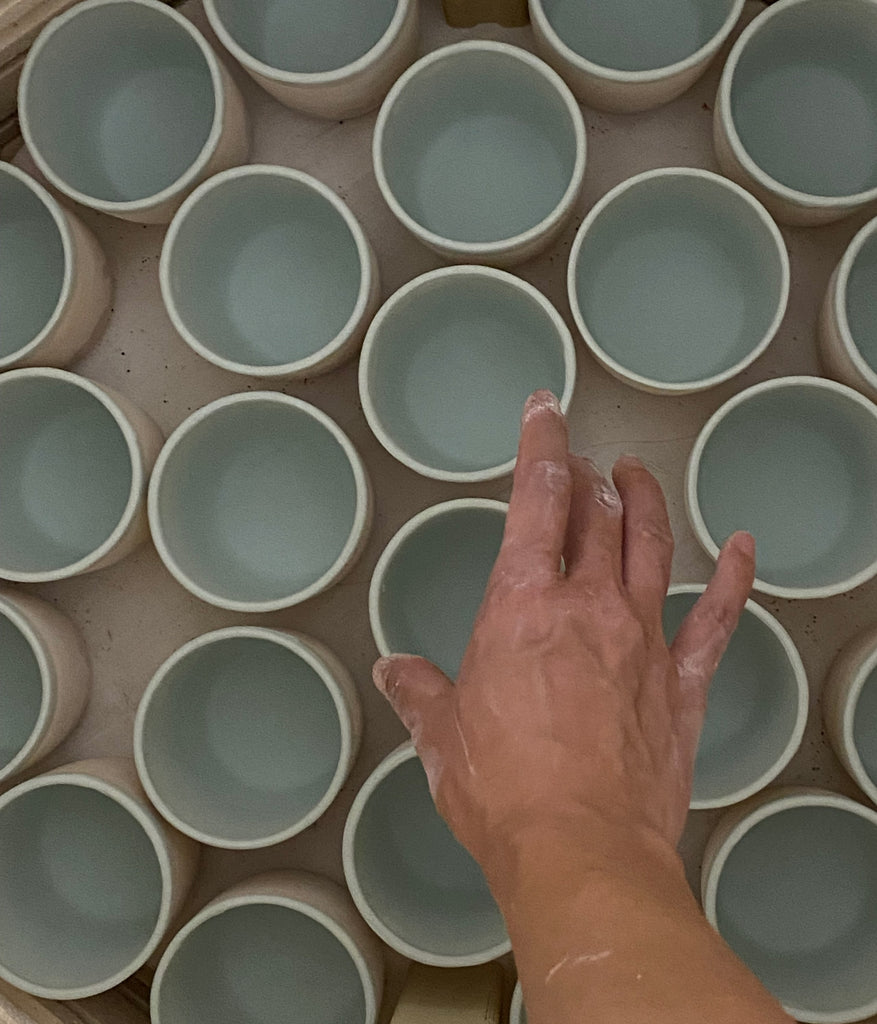 Photo of Karen's hand in the kiln with all the LA mugs