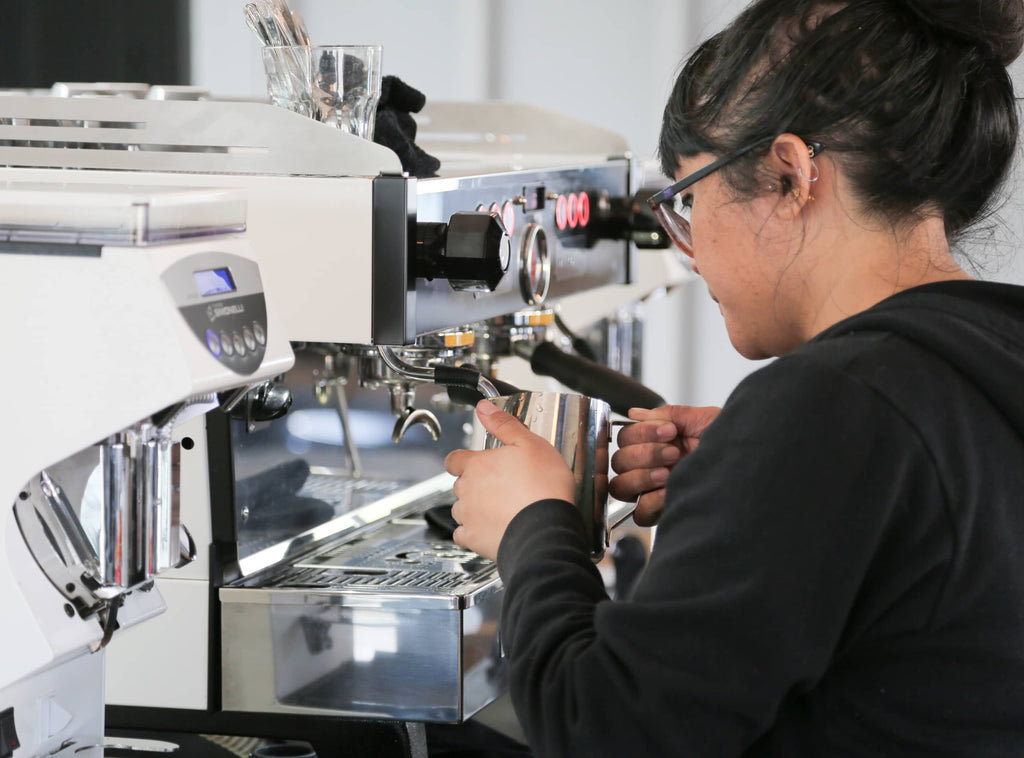 Photo of a person steaming milk at an espresso machine.