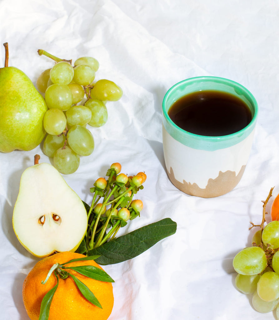 Photo of the LA mug next to pears, grapes, a clementine, and some small flowers.