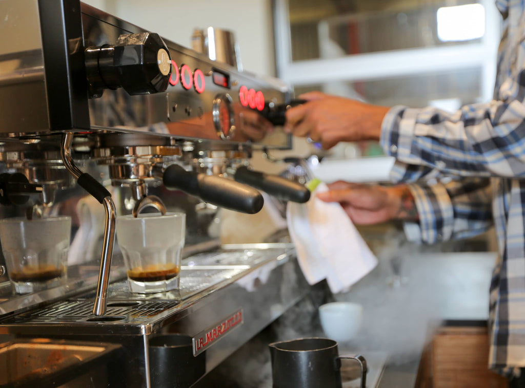 Photo of a person wiping a steam wand on an espresso machine.