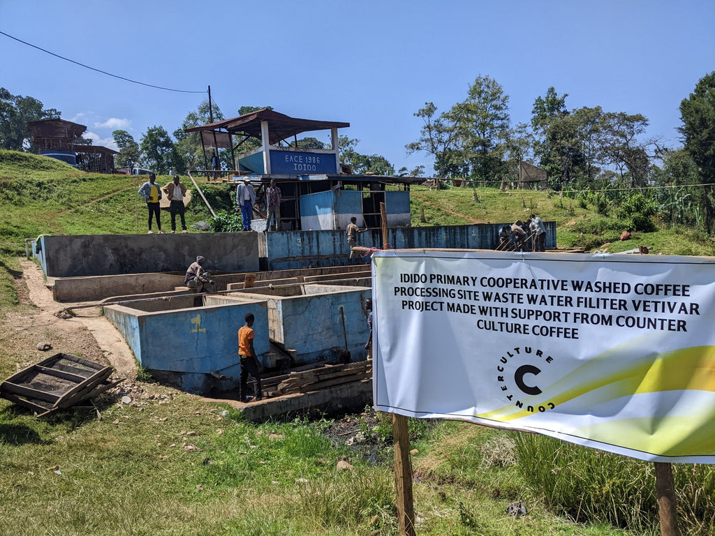 Photo of the Idido washing station in Ethiopia with a banner out that reads, "Idido primary cooperative washed coffee processing site waste water filter vetivar project made with support from Counter Culture Coffee."
