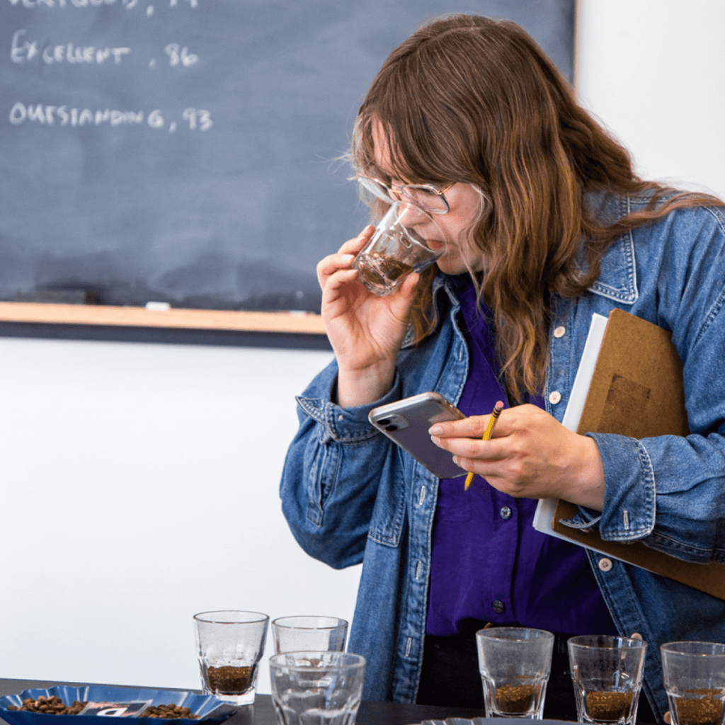 Photo of a person sniffing coffee beans in a glass.