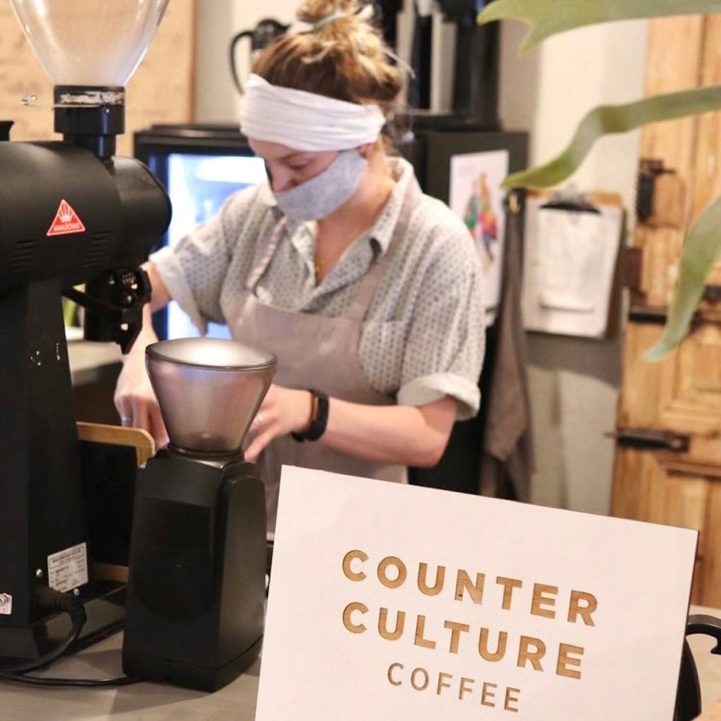 Photo  of a person brewing coffee with a sign in front that reads, "Counter Culture Coffee."