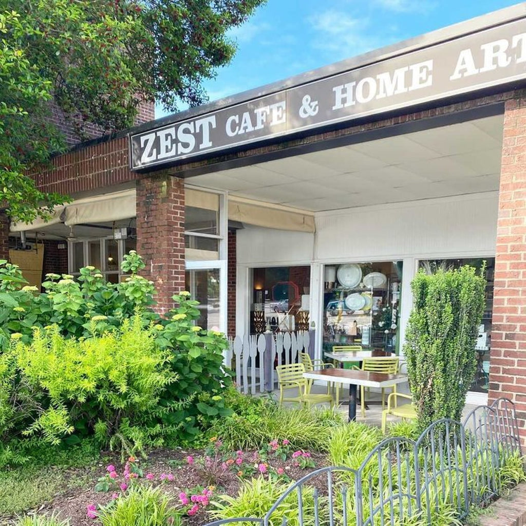 Photo of the exterior of Zest Cafe & Home Arts. There are exterior plants, seats, and a sign with the name of the business. 