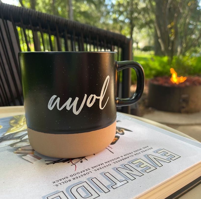 Photo of a mug that says AWOL sitting on a book outside.