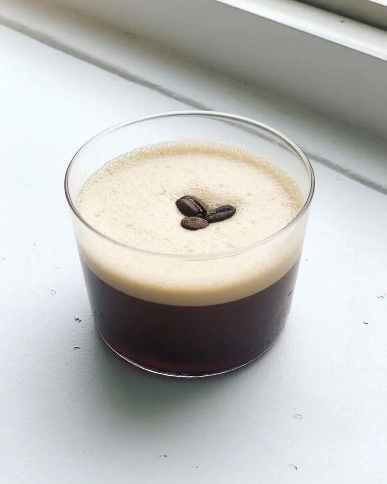 Photo of an espresso martini in a rocks glass. There are three coffee beans in the middle on the foam. 