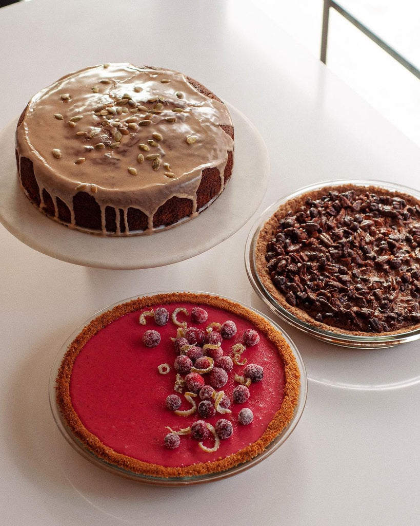 Photo of three desserts on a white surface. One is a cake and the other two are pies.