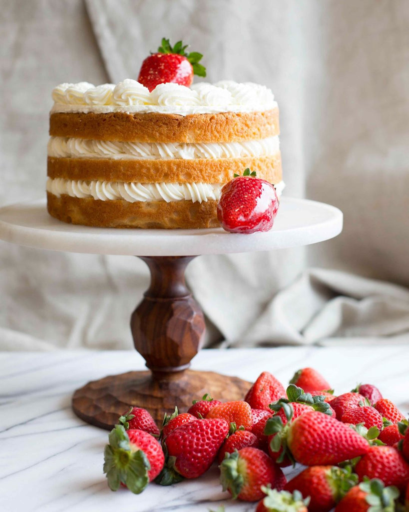 Photo of a layered cake on a stand with strawberries next to it. 