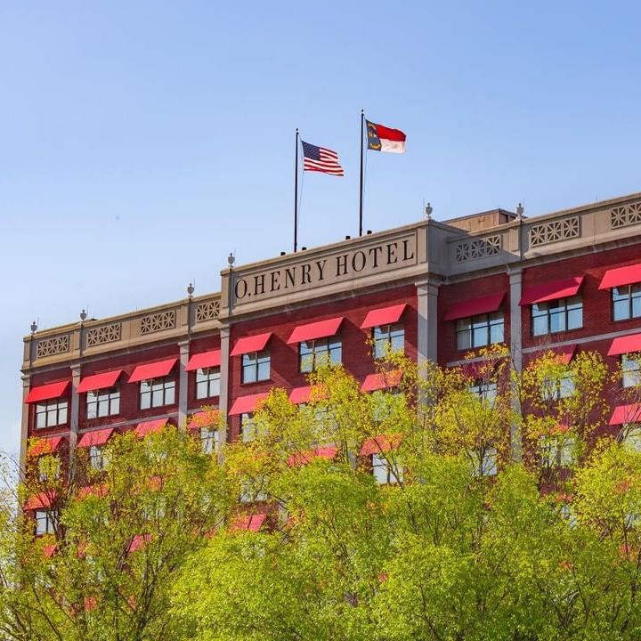 Exterior of the O'Henry Hotel with flags on the top and green trees covering the foreground. 