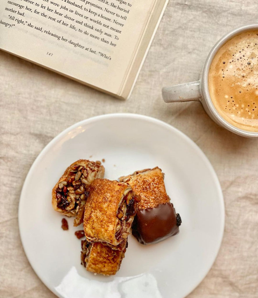Top down photo of a plate of rugelach next to a latte and book.