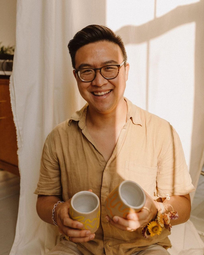 Photo of Sonny smiling at the camera and holding a mug in each hand.