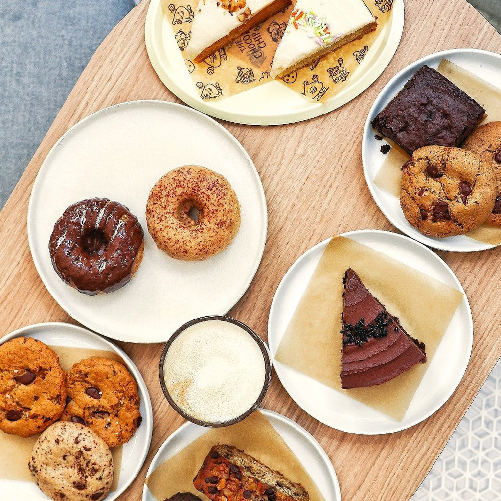 Top down photo of plates with various desserts on a wooden surface with a latte in the middle.