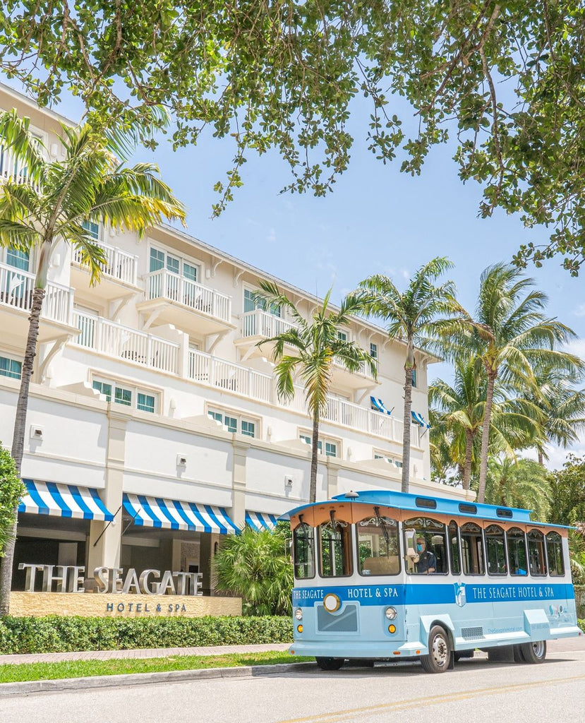 Photo of a trolly in front of the Seagat Hotel and Spa. You can see striped awning and palm trees adorning the hotel. 