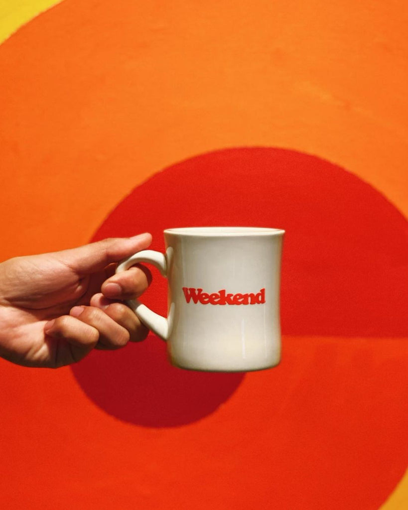 Photo of a hand holding a mug of coffee. The mug says, "Weekend" on it. 