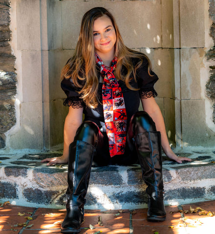 woman with long hair sitting at a fountain wearing all black with a red krampus scarf