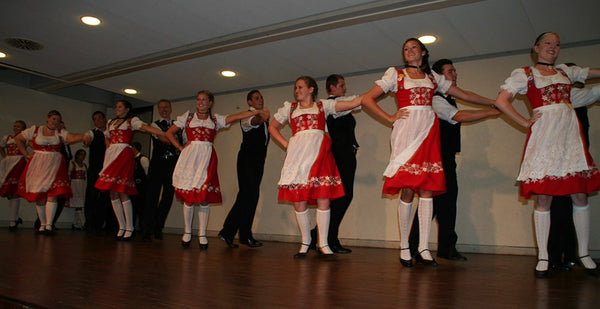 Group of young people doing traditional German folk dance, wearing red german dirndl with white aprons 