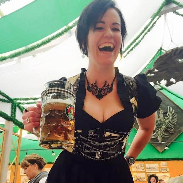 woman with a short haircut wearing traditional oktoberfest clothing with dirndl skirt and dirndl blouse, large black necklace laughing and holding a liter of beer in a beer tent at Okotoberrfest in Munich