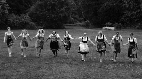 a group of women running in a field holding hands wearing dirndls in germany