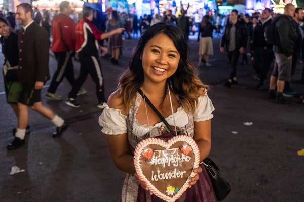 Woman wearing a handmade dirndl at Oktoberfest in munich holding a large lebkuchenherz in front of the oktoberfest beer tents