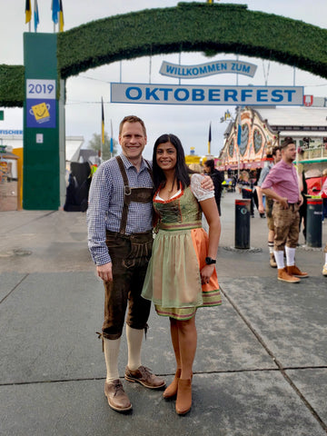 a man in lederhosen with his arm around a woman wearing a custom made dirndl at oktoberfest. these are typical oktoberfest outfits for modern times