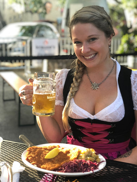 Girl with braided hair, having a meal with a drink, wearing a dirndl