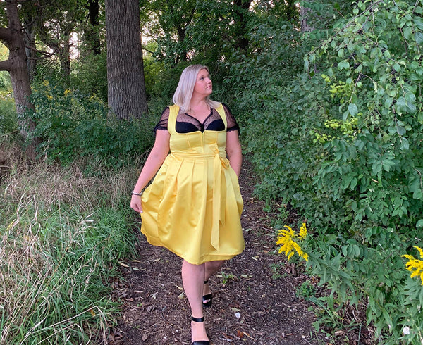 Woman walking through the forest, wearing high fashion yellow Dirndl, and black blouse and high heels