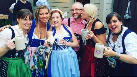 group of people smiling wearing authentic german dirndl dresses and lederhosen at an oktoberfest party